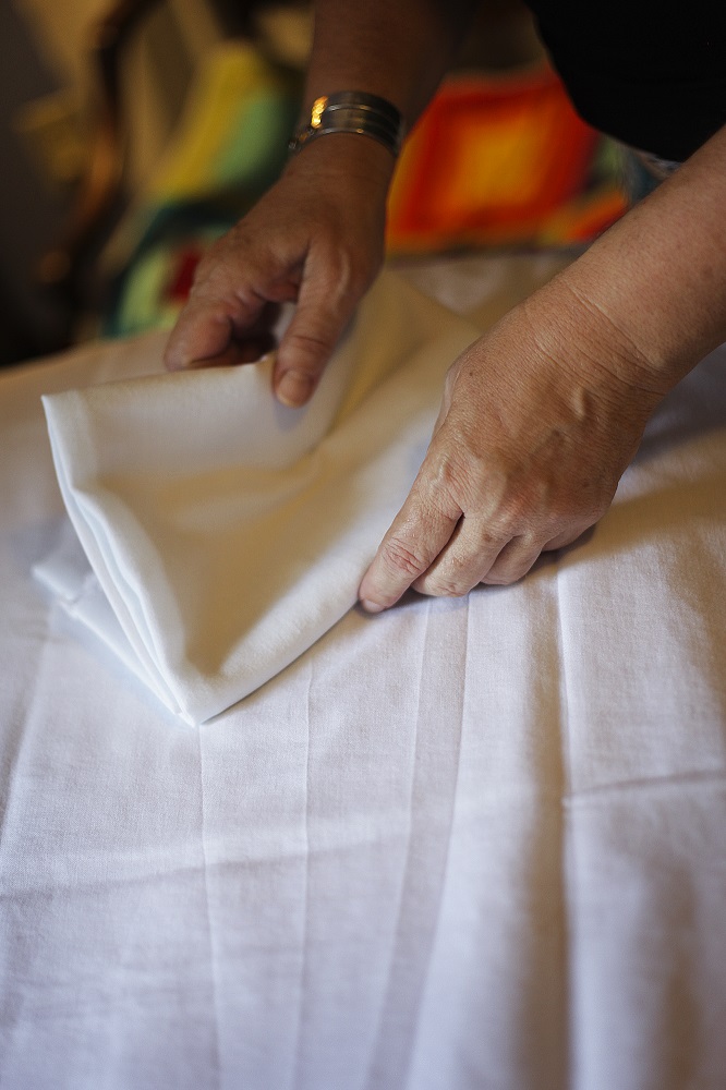 [Photo: Angy Nixon folds a sheet on top of an exam table in her home office.]