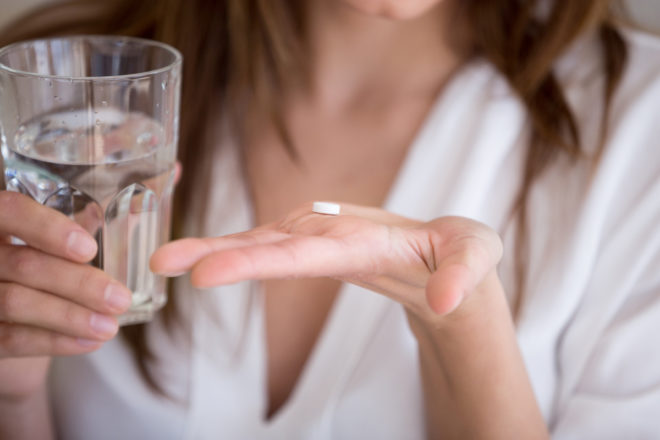 [Photo: Person holding glass of water and pill in hand.