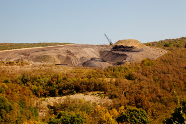 [Photo: Heavy machinery mining coal using mountain removal in front of a patch of woods.]