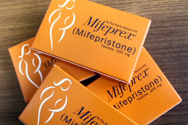 [Photo: Orange boxes of Mifeprex (mifepristone) lie on top of one another on a table.]