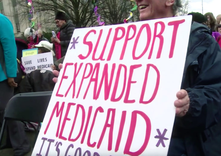 [Photo: Medicaid expansion supporters hold signs during a rally.]